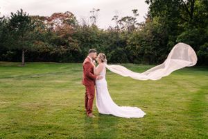 Dramatic wedding photo with flowing veil catching wind on green lawn.