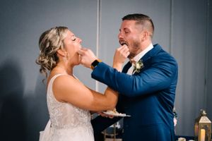 Wedding couple laughs while playfully feeding each other cake at their reception.
