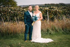 Elegant wedding couple standing in field with teal and white floral bouquet.
