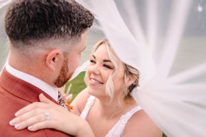Candid wedding moment captured under flowing white veil with joyful expressions.