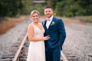 Elegant couple in wedding attire poses together on rustic train tracks.