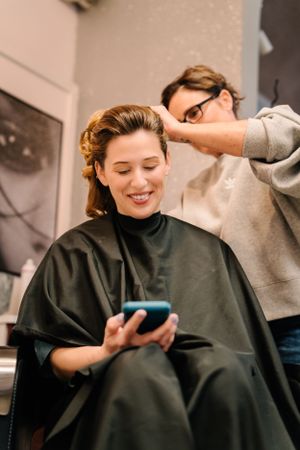 Client checking phone while getting hair styled at salon.