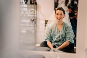 A candid getting ready moment before the wedding shows a person in a mint robe smiling in a salon mirror.