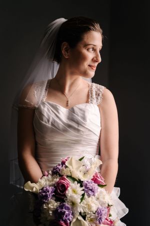 A bride in a white wedding gown poses for a dramatic portrait against a dark background.