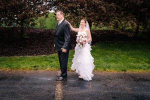 A couple participates in their first look moment on a wet path near autumn foliage.
