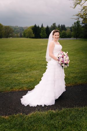 A bride in a flowing white dress poses on a path with pink and purple bouquet.