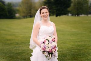 A bride smiles brightly while holding her floral bouquet on her wedding day.