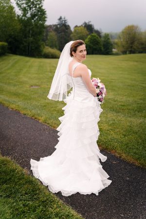 A bride in a cascading white gown poses on a paved path surrounded by rolling hills.
