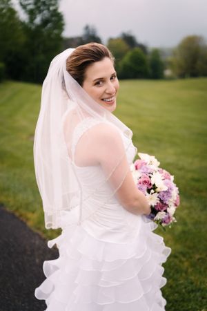 A bride glances over her shoulder with a bright smile on a garden path.