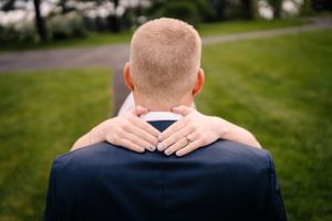 Close-up of hands embracing around shoulders in navy suit jacket.
