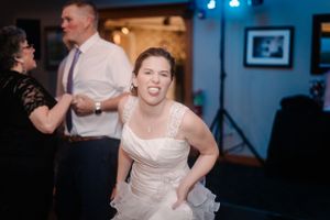 A bride dances joyfully at her wedding reception with blue stage lights in the background.