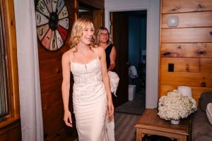 Person in an elegant white satin wedding dress standing in a rustic cabin interior.