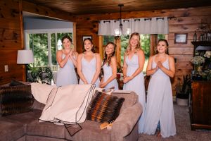 Bridesmaids in matching pale dresses reacting with excitement in a rustic cabin setting.