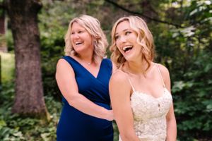 A bride in a white gown shares a joyful laugh with a woman in a navy blue dress during a wedding celebration.