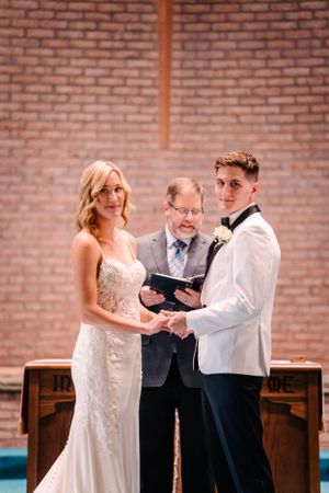 A wedding ceremony in a brick-walled church with a couple exchanging vows before an officiant.