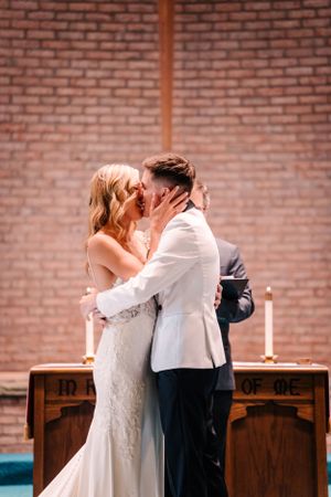 Newlyweds share their first kiss as a married couple at a church altar with brick walls.
