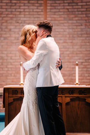 A romantic first kiss between newlyweds at the altar with lit candles in the background.