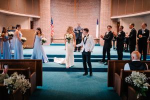 Wedding party stands in a church with light blue bridesmaids and white floral decorations.