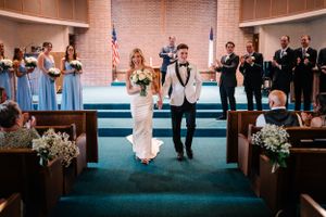 Wedding ceremony in a church with light blue bridesmaids and floral decorations along the aisle.