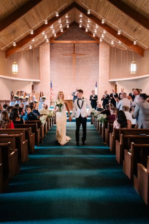 Newlyweds walk down the aisle in a church with string lights and wooden pews.