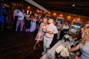 Wedding guests dance and celebrate on a wooden dance floor with decorative lighting.