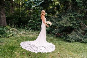 A bride in a fitted lace gown with dramatic train poses in a garden setting.