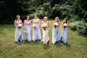 Wedding party in light blue and white dresses pose together on grass with bouquets.