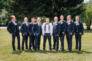 Groomsmen lined up outdoors wearing matching navy suits with central figure in white formal attire.