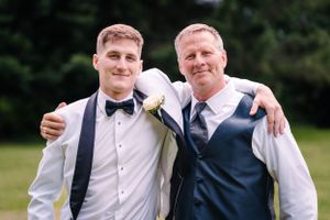 Casual outdoor portrait of two men in formal attire embracing at a wedding.