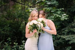Two wedding party members laugh together while holding their floral bouquets.