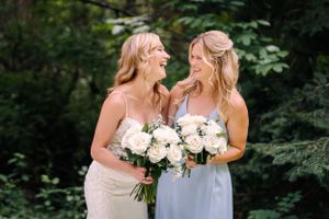 Two wedding attendants share a candid laughing moment while holding cream rose bouquets.
