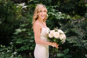 A bride poses with her white rose bouquet in a garden setting.