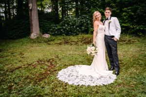 Elegant outdoor wedding portrait featuring couple on green lawn with bride's long lace train.
