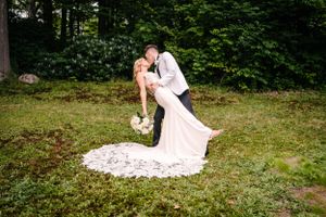 Dramatic dip pose with bride's lace train spread beautifully on garden grass.