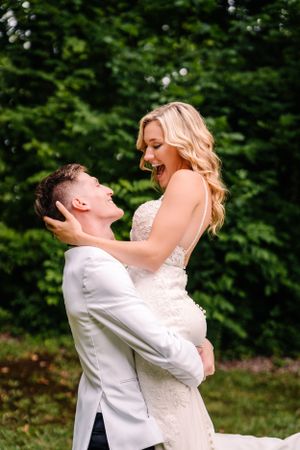 Joyful wedding couple sharing playful lift moment against forest backdrop.