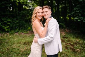 A romantic wedding photo of a couple embracing outdoors with a lush forest backdrop.