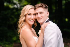 Close-up portrait of newlyweds smiling together against green foliage.