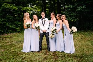 Wedding party photo with bridesmaids in light blue dresses and central figure in white tuxedo.