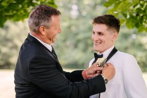 Special moment captured as older gentleman helps with groom's formal attire.