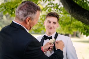 Wedding preparation scene showing final adjustments to groom's formal wear outdoors.