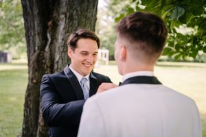 Candid moment of wedding preparations as groomsmen fix formal attire details.