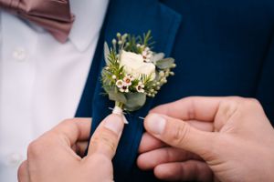 Close-up of hands pinning a white and green boutonniere onto a navy suit lapel.