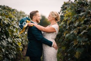 Romantic embrace between newlyweds with blue bouquet in vineyard setting.