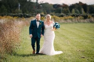 A couple walks across a grassy field on their wedding day, with the bride in white and groom in navy.