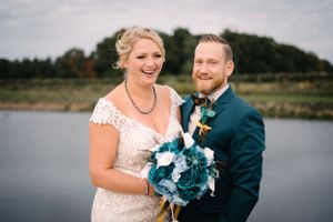Joyful wedding couple shares genuine laughter during outdoor lakeside portraits.