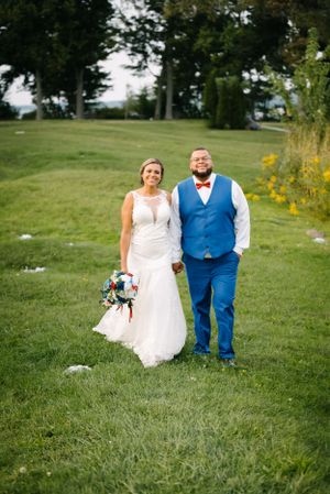 Happy newlyweds pose on grassy hill with yellow wildflowers in background.