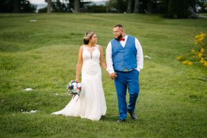 Newlyweds walk together on lush green lawn during summer wedding celebration.