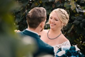 Happy bride in lace dress and necklace smiling during outdoor wedding photoshoot.