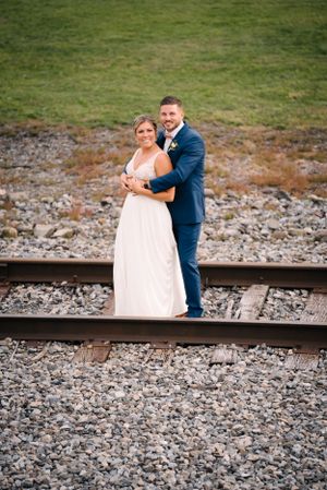 Wedding couple embraces while standing on railroad tracks against natural background.