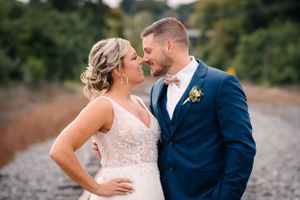 Newlywed couple in formal attire share intimate moment on railroad tracks.